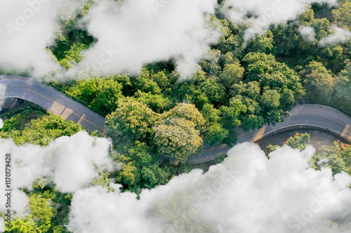 Aerial top view of electric vehicle driving on a winding highway road in green forest with fog. Sustainable transportation, zero emissions, and eco-friendly mobility for reducing carbon footprints. photo