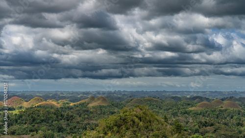 Rows of unusual rounded hills covered with brownish grass stretch to the horizon. Lush tropical vegetation in the valley. Clouds in the sky. Philippines. Bohol.Chocolate Hills Natural Monument.Carmen