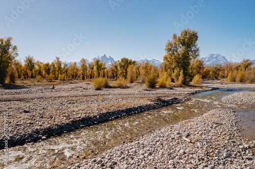 Autumnal stream flows through a rocky bed, with snow-capped Teton mountains in the background. Peaceful, scenic landscape. Grand Teton National Park, Moran, Wyoming, USA. photo