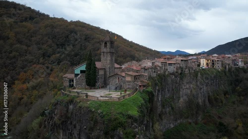 Castellfollit de la Roca catalan town with little houses, cliffs and San Salvador church in Catalonia, Spain. High quality 4k drone footage