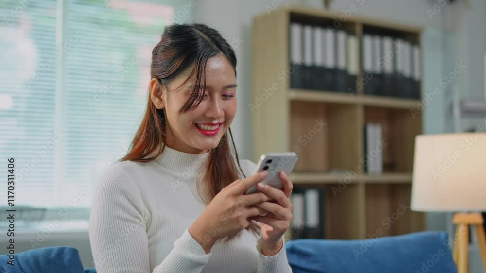 Attractive Asian woman Smiling while talking on the cell phone with co-workers, shopping online. Happy chatting while relaxing on the sofa in the living room at home. Holiday concept. Attractive Asian woman Smiling while talking on the cell phone with co-workers, shopping online. Happy chatting while relaxing on the sofa in the living room at home. Holiday concept.