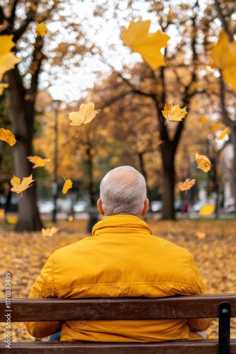  Elderly man in yellow jacket sitting on bench as autumn leaves fall. Back view photography capturing motion and peaceful autumn setting. photo