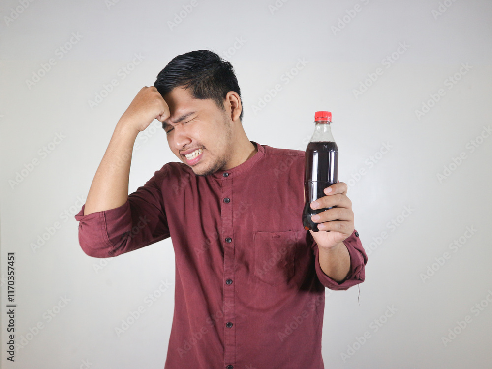 Asian man is holding a soft drink with a disappointed expression while patting his forehead Asian man is holding a soft drink with a disappointed expression while patting his forehead