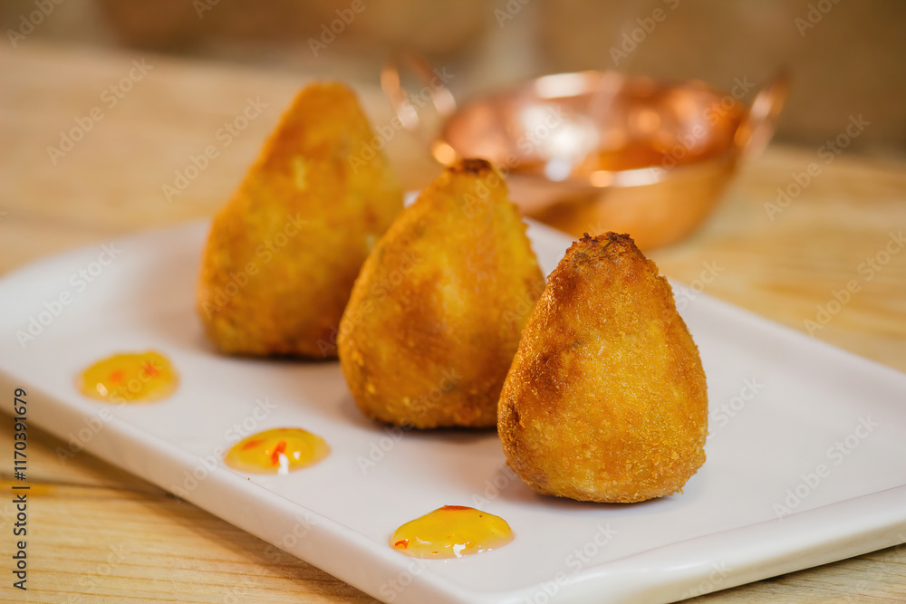 drumsticks of various flavors on a white plate with a bronze pan behind on a wooden table with texture close-up photo with texture drumsticks of various flavors on a white plate with a bronze pan behind on a wooden table with texture close-up photo with texture