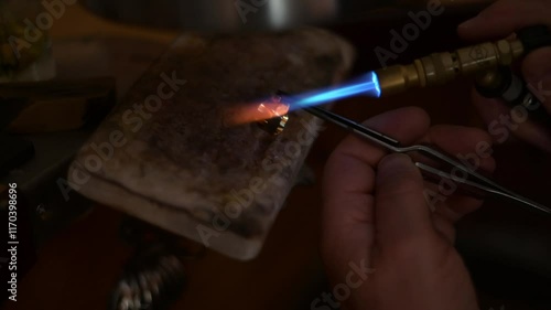 Professional jeweler refining golden ring, welding blowtorch and tweezers during meticulous metalworking process, showcasing precision craftsmanship with detail. Experienced goldsmith