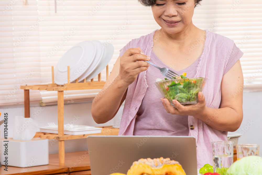 Senior Asian woman with short gray hair preparing healthy food in kitchen, using laptop listen to music or salad recipe research, modern lifestyle silver hair female in 70s friendly with technology Senior Asian woman with short gray hair preparing healthy food in kitchen, using laptop listen to music or salad recipe research, modern lifestyle silver hair female in 70s friendly with technology