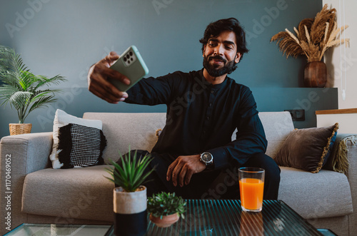 Pakistani young man using smart phone on the couch.