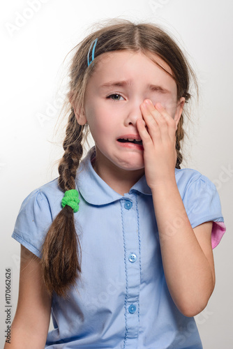 Fotografie A close-up shot of a young girl with pigtails, wearing a light blue shirt, visibly upset and crying
