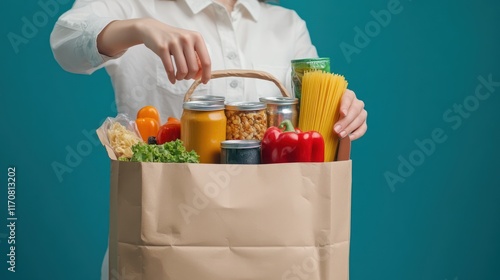 Woman holding a paper grocery bag filled with various food items against a teal background. photo