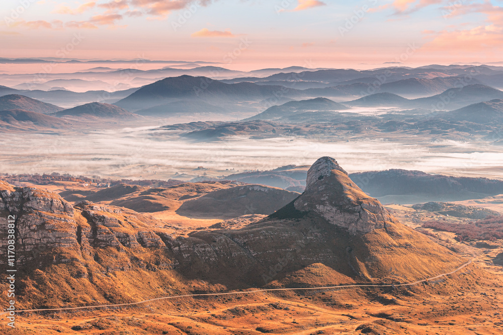 Stunning sunrise paints the sky with vibrant colors over a foggy valley nestled amidst the rugged peaks of Durmitor national park, Montenegro