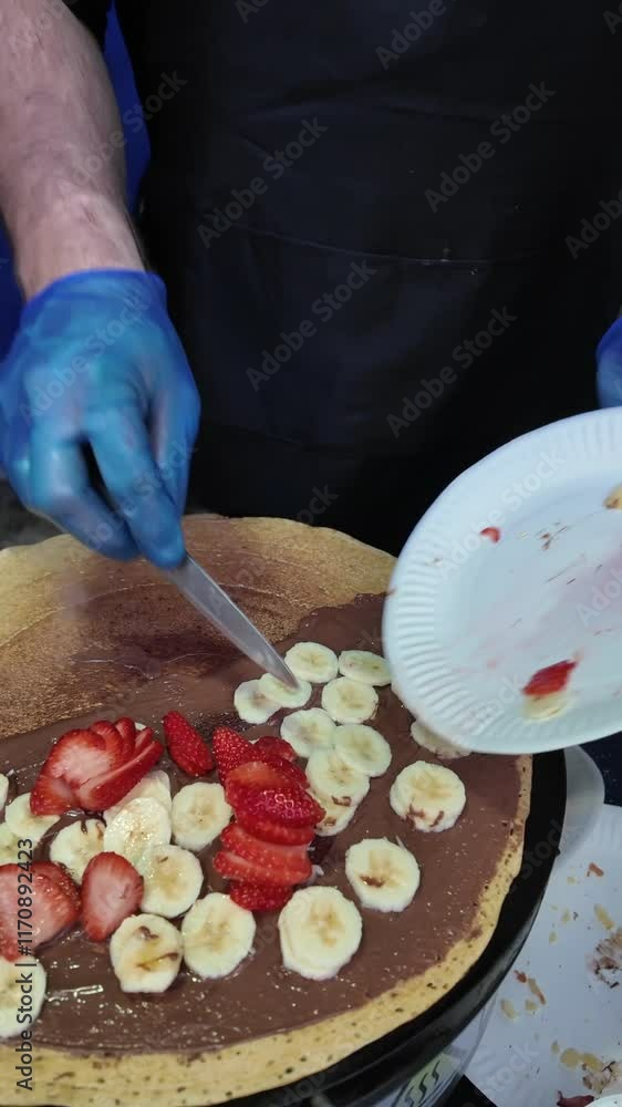 A man is making a dessert with bananas and chocolate. He is wearing gloves and apron. The dessert is in a pan and has bananas on top