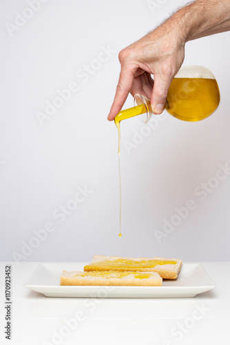A hand drizzling extra virgin olive oil on a plate with bread. Copy space.