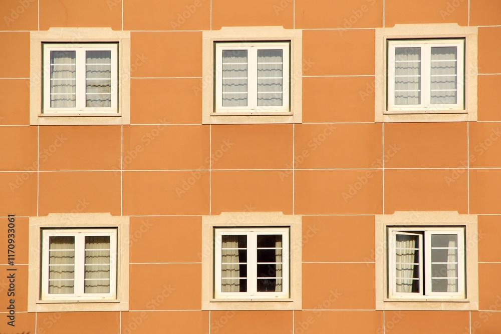 Fototapeta premium Symmetrical facade of an orange building with six white-framed windows.