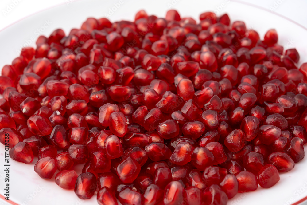 Gennevilliers, France - 01 02 2024: Close up of a white plate filled with red triangular pomegranate seeds on a white background. Gennevilliers, France - 01 02 2024: Close up of a white plate filled with red triangular pomegranate seeds on a white background.