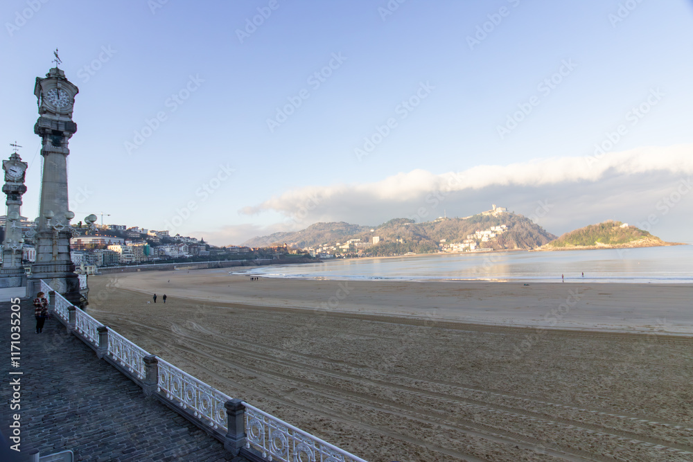 Sandy beach with waterfront buildings and hills in the background at sunset in San Sebastian, Spain. Coastal cityscape and natural landscape. Sandy beach with waterfront buildings and hills in the background at sunset in San Sebastian, Spain. Coastal cityscape and natural landscape.
