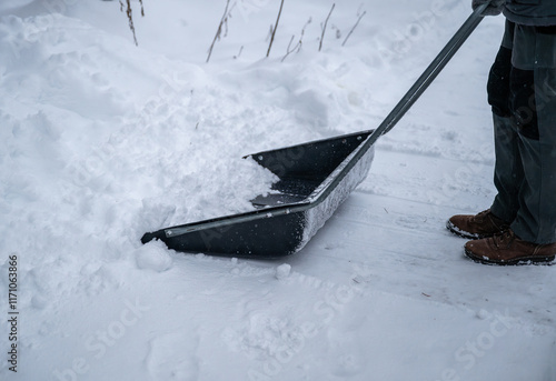 person clearing snow with a large snow shovel on a snowy pathway. concept of outdoor chores	 photo