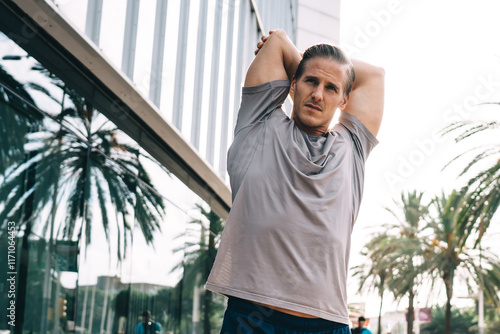 Determined male athlete stretching body during morning training in urbn city, Caucasian jogger in sportswear concentrated on intensity practice keeping perfect shape and healthy lifestyle photo