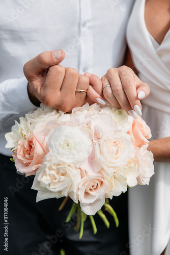 A pair of hands of lovers with golden wedding rings on a background of bouquet flowers.