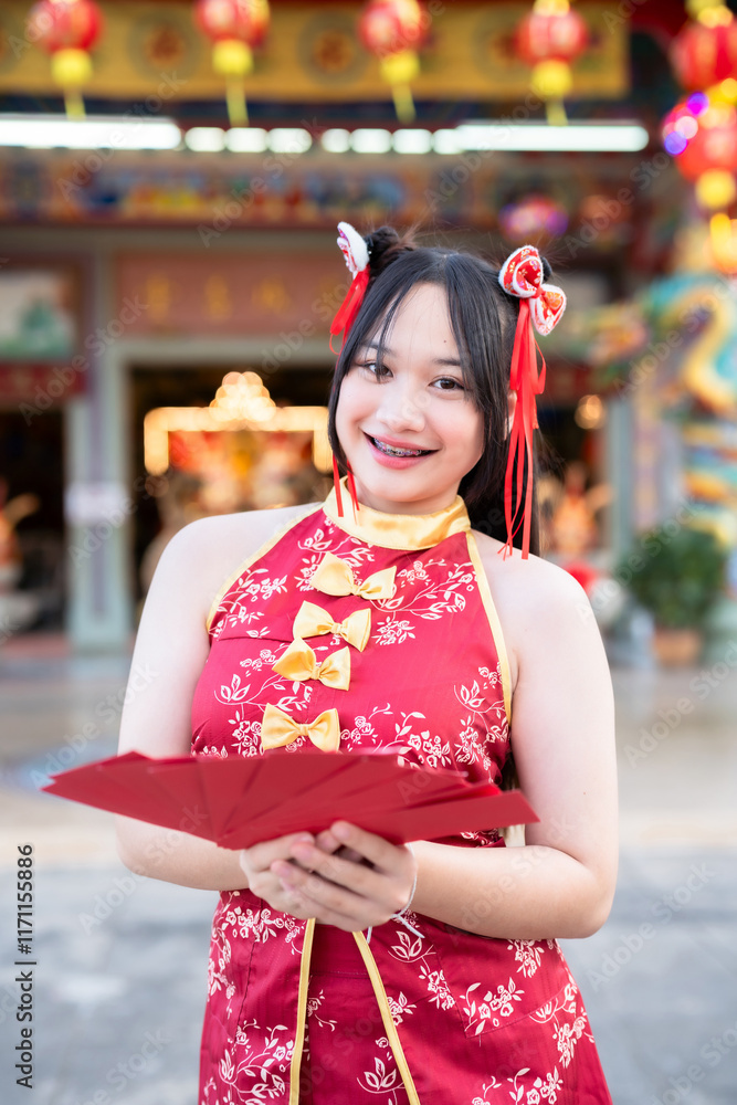Portrait smiles Asian young woman wearing red cheongsam dress holding red envelopes decoration for Chinese new year festival celebrate culture of china at Chinese shrine Public places in Thailand