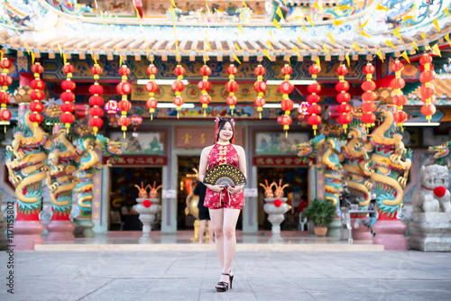 Portrait beautiful cute smiles Asian young woman wearing red traditional Chinese cheongsam decoration and holding a Chinese Fanning for Chinese New Year Festival at Chinese shrine in Thailand