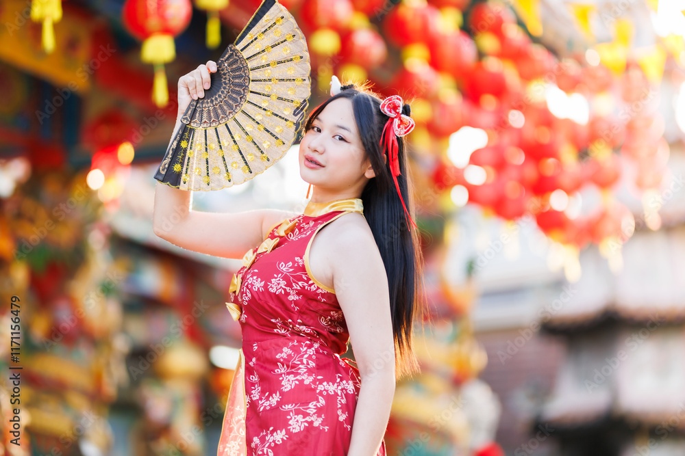 Portrait beautiful cute smiles Asian young woman wearing red traditional Chinese cheongsam decoration and holding a Chinese Fanning for Chinese New Year Festival at Chinese shrine in Thailand