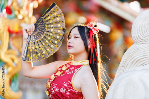 Obraz na płótnie Portrait beautiful cute smiles Asian young woman wearing red traditional Chinese cheongsam decoration and holding a Chinese Fanning for Chinese New Year Festival at Chinese shrine in Thailand w salonie