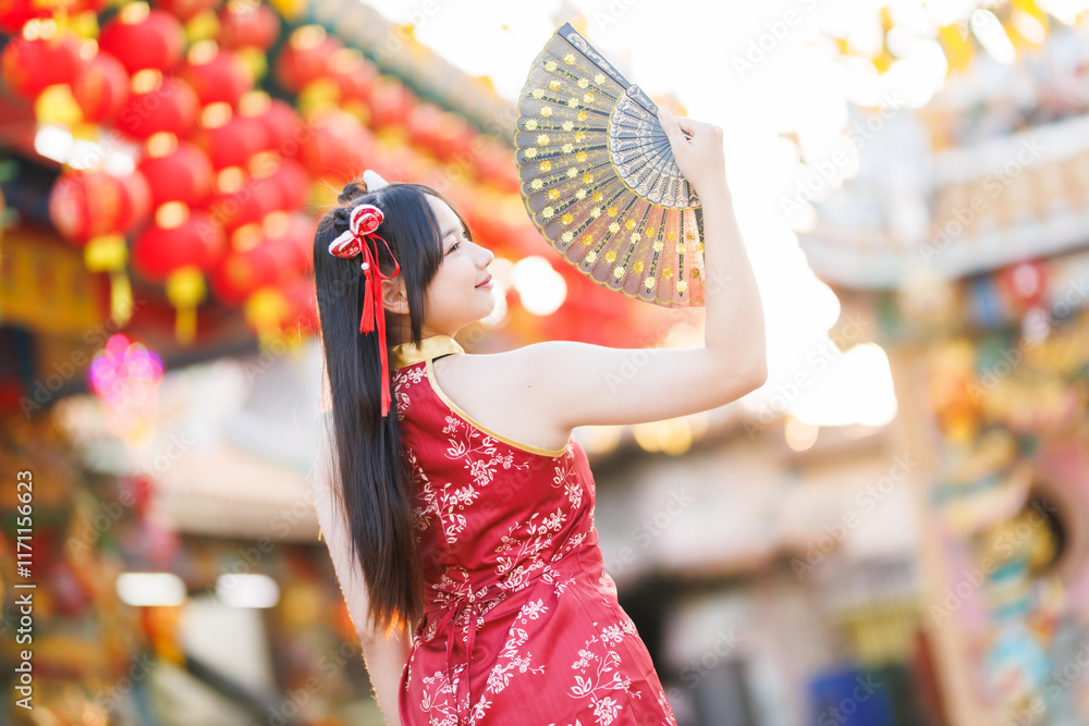 Portrait beautiful cute smiles Asian young woman wearing red traditional Chinese cheongsam decoration and holding a Chinese Fanning for Chinese New Year Festival at Chinese shrine in Thailand