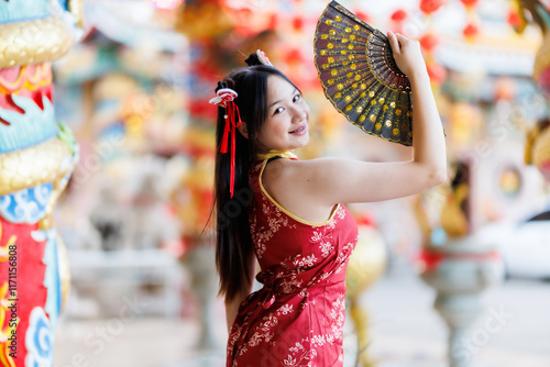 Obraz na płótnie Portrait beautiful cute smiles Asian young woman wearing red traditional Chinese cheongsam decoration and holding a Chinese Fanning for Chinese New Year Festival at Chinese shrine in Thailand w salonie