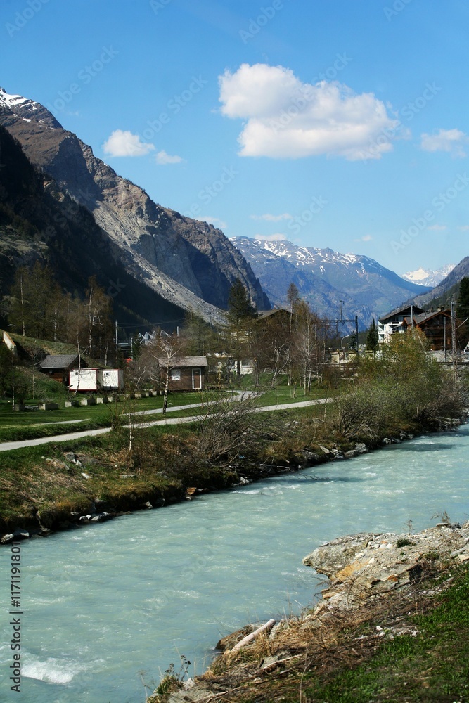 Fototapeta premium River flowing through a quaint village with mountains in the background. Zermatt, Switzerland