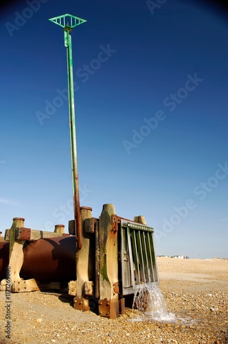 Sewage oulet on a gravel beach, with water coming out of the pipe. photo