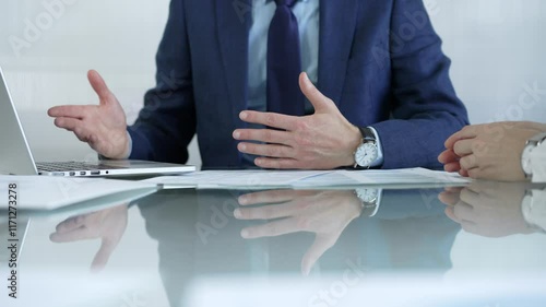 Business partners or lawyers dressed in blue are reviewing contract terms during a meeting, using a laptop and documents on a glass table. Businesspeople theme