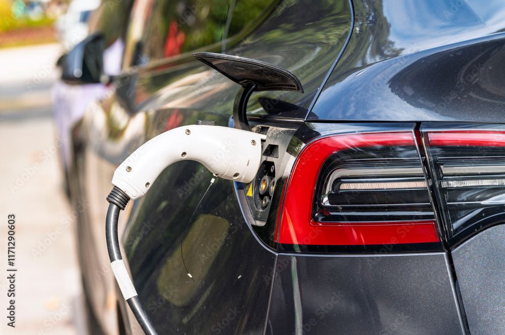 Closeup EV Car charger handle plugged in recharging EV car battery from EV charging station with green nature background. Eco-friendly alternative energy concept