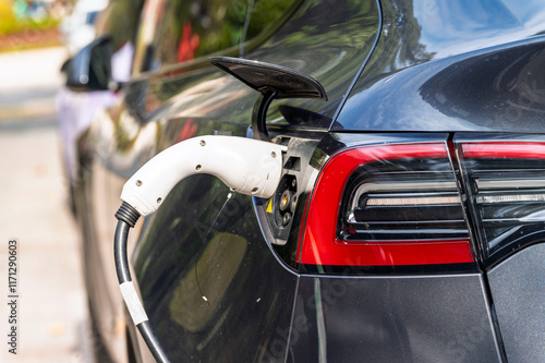 Obraz na płótnie Closeup EV Car charger handle plugged in recharging EV car battery from EV charging station with green nature background. Eco-friendly alternative energy concept w salonie