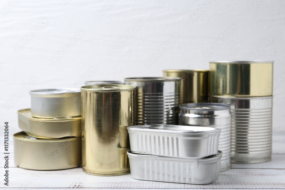 Many closed tin cans on white wooden table, closeup Many closed tin cans on white wooden table, closeup