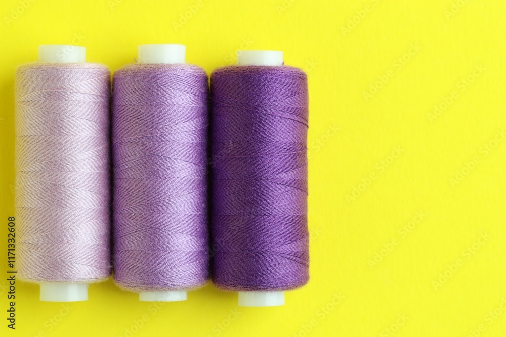 Spools of colorful sewing threads on yellow background, flat lay. Space for text Spools of colorful sewing threads on yellow background, flat lay. Space for text