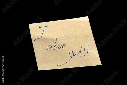 Yellow adhesive paper, similar to a Post-it note, on a black background with the words “I Love You” handwritten in blue ink.