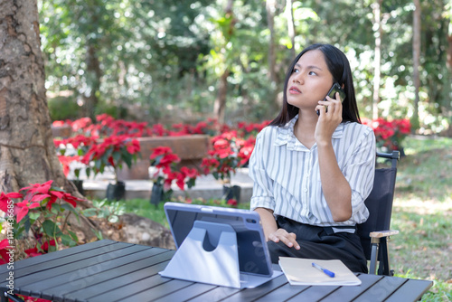 Troubleshooting on the phone, stressed Asian woman feeling overwhelmed and trying to solve a problem While talking long distance via mobile phone remote network Complete with a tablet on table. photo