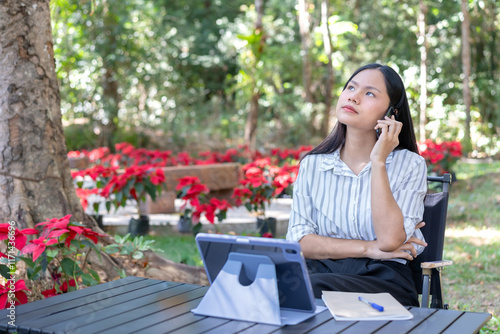 Troubleshooting on the phone, stressed Asian woman feeling overwhelmed and trying to solve a problem While talking long distance via mobile phone remote network Complete with a tablet on table. photo