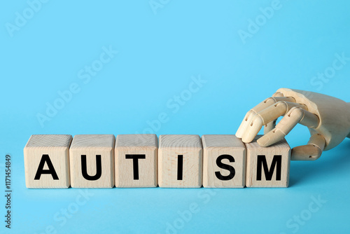 Word Autism made of wooden cubes and mannequin hand on light blue background, space for text photo