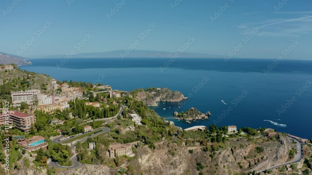 Aerial orbit drone shot over the historic town of Taormina. Buildings at the foot of the rocky mountains in Sicily overlooking Mediterranean sea cost. Aerial orbit drone shot over the historic town of Taormina. Buildings at the foot of the rocky mountains in Sicily overlooking Mediterranean sea cost.