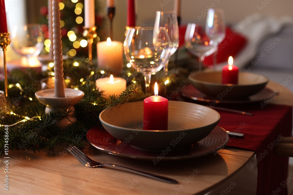 Beautiful dishware with burning candles, fir tree branches and Christmas lights on wooden table indoors, closeup Beautiful dishware with burning candles, fir tree branches and Christmas lights on wooden table indoors, closeup