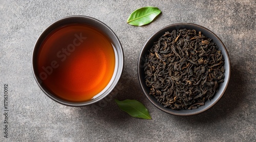 Black tea served in a cup with fresh tea leaves and loose tea on a dark surface