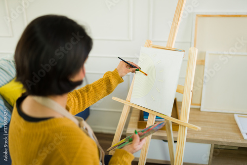 Female artist painting colorful canvas, wielding paintbrush and palette, working intensely in bright home studio setting photo