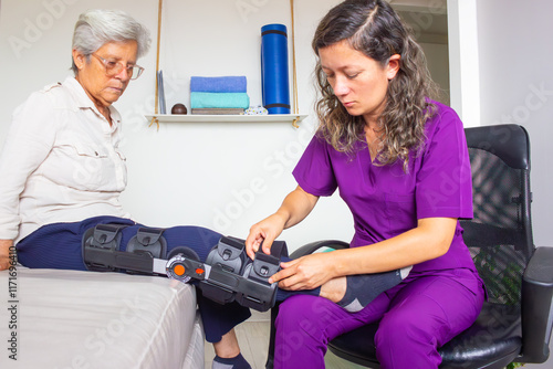 Fotografie Elderly patient receiving care from a physiotherapist adjusting her knee immobilizer in a health clinic setting, emphasizing support and rehabilitation