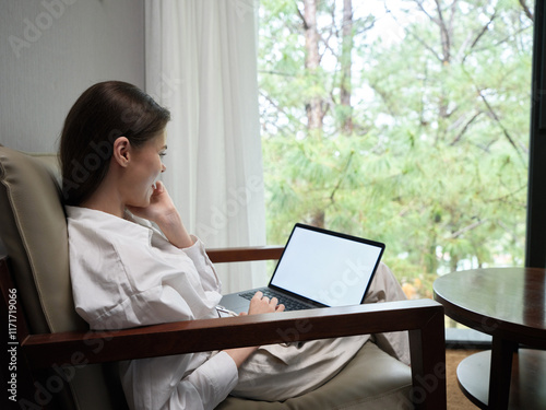 Woman in a cozy robe using a laptop while sitting by a window  blending nature with modern technology  peaceful and relaxed atmosphere