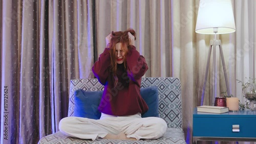 Young red-haired woman screams in hysterics and pulls out her hair from despair, anger, sadness and loneliness