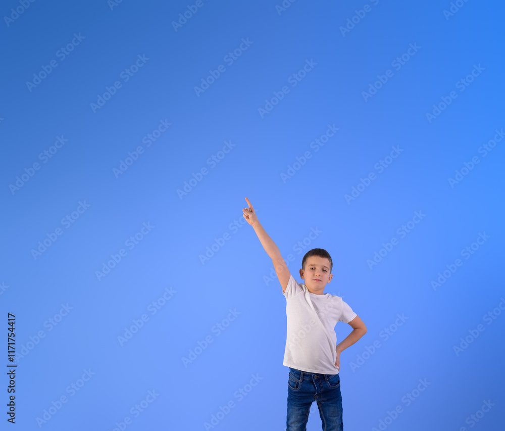 Portrait of confident boy pointing up at copy space for advertisement while standing on blue background Portrait of confident boy pointing up at copy space for advertisement while standing on blue background