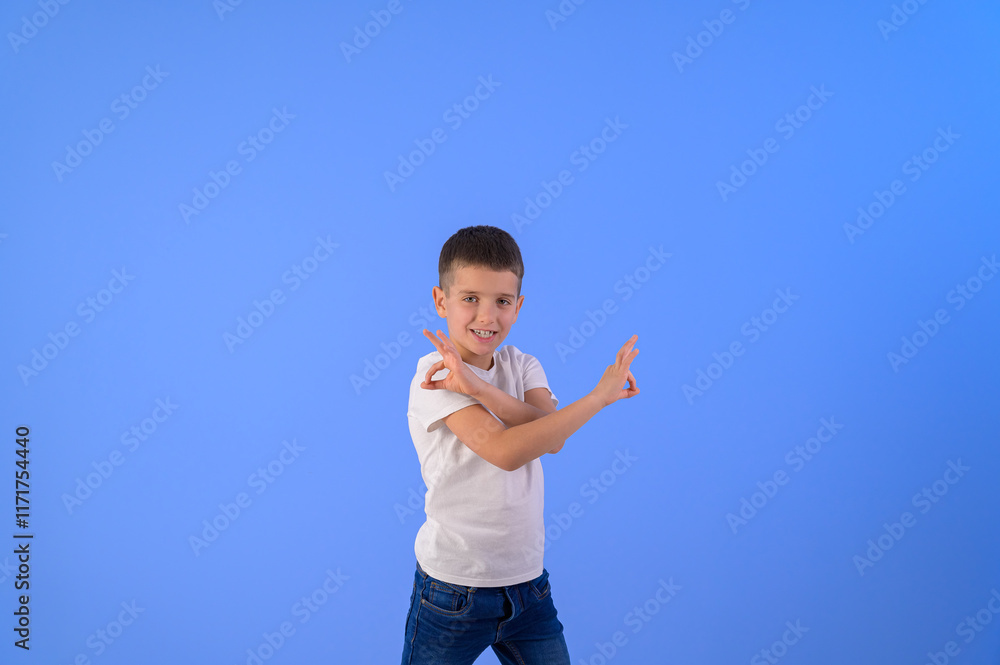 Portrait of cute boy crossing hands and showing OK signs while standing on isolated blue background Portrait of cute boy crossing hands and showing OK signs while standing on isolated blue background