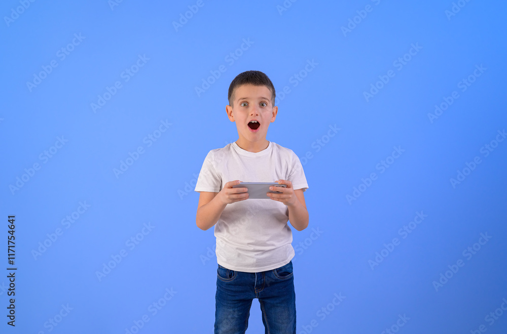 Portrait of shocked boy with mouth open playing video game over mobile phone over blue background