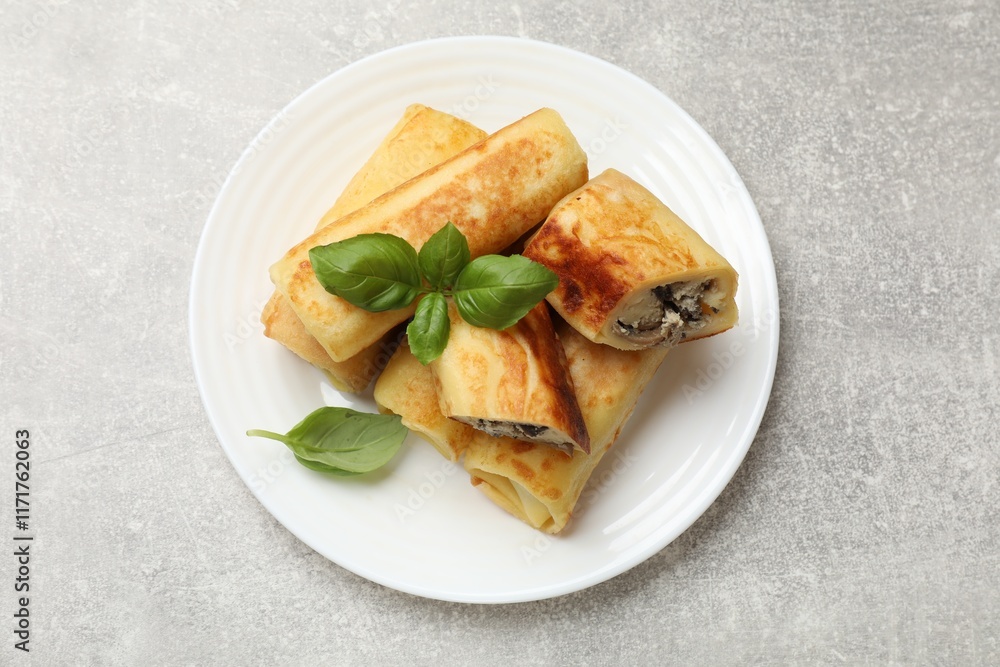 Delicious rolled crepes with mushrooms and basil on grey table, top view